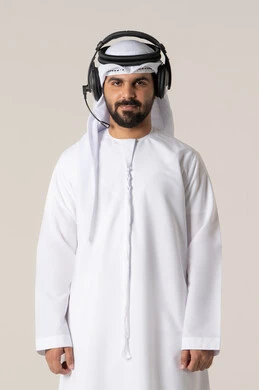 Spending a comfortable and enjoyable time through headphone technology, following music and entertainment with headphones, listening to musical clips, wearing audio headphones, a portrait of an Arab Gulf Emirati man wearing the Emirati kandura, listening to songs with gestures of joy and happiness, white background.
