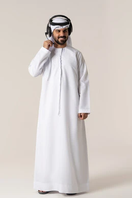 Listening to music and entertainment with headphones, enjoying musical clips, wearing audio headphones, a portrait of an Arab Gulf Emirati man wearing the Emirati kandura, listening to songs with gestures of joy and happiness, full-body shot, white background.