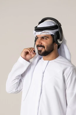 Enjoying listening to songs, entertainment and fun using headphone technology, wearing audio headphones, a portrait of an Arab Gulf Emirati man wearing the Emirati kandura listening to songs with gestures of joy and happiness, white background.