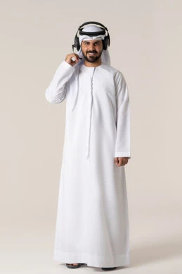 Listening to music clips, entertainment and fun using headphone technology, wearing audio headphones, a portrait of an Arab Gulf Emirati man wearing the Emirati kandura listening to songs with gestures of joy and happiness, full-body, white background.