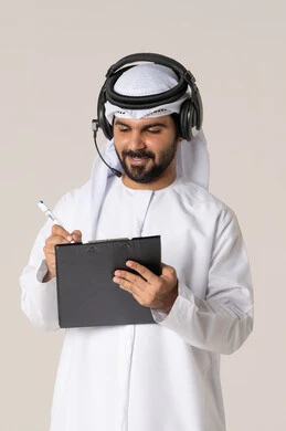 Documenting ideas and data in a paper notebook, organizing and managing tasks, writing daily tasks and goals, a portrait of a smiling young Emirati Arab man wearing a kandura and a white ghutrah, with headphones, holding a folder and a pen in his hand, white background.