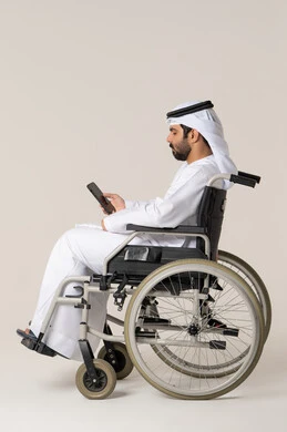 الاطلاع على البرامج والتطبيقات الخاصة بالتسوق عبر الجوال، بورترية من الجانب لرجل عربي خليجي اماراتي من ذوى الاحتياجات الخاصة يرتدي الدشداشة و الغترة البيضاء يجلس على كرسي متحرك يحمل الهاتف المحمول، تطور التكنولوجيا والأجهزة التقنية، الدردشة مع الأهل والأصدقاء، إيماءات الاندماج والتركيز، خلفية بيضاء