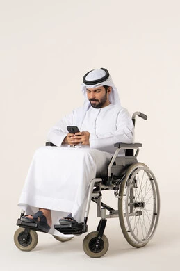 تصفح تطبيقات الجوال الخاصة بالشراء الإلكتروني، بورترية لرجل عربي خليجي اماراتي من ذوى الاحتياجات الخاصة يرتدي الدشداشة و الغترة البيضاء يجلس على كرسي متحرك يحمل الهاتف المحمول، تطور التكنولوجيا والأجهزة التقنية، الدردشة مع الأهل والأصدقاء، إيماءات الاندماج والتركيز، خلفية بيضاء