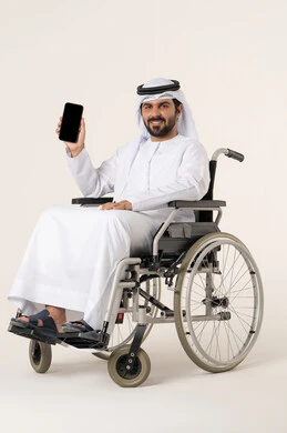 Integrating modern technology with daily activities, looking at the camera with gestures of happiness and joy, a portrait of a young Emirati Arab man with special needs wearing a kandura and a white ghutrah sitting in a wheelchair and holding a mobile phone, displaying a blank black screen on the phone, white background.