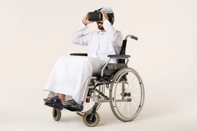 Integration and simulation of the imaginary world, a portrait of a young Emirati Arab with special needs wearing traditional attire and 3D glasses (VR), sitting in a wheelchair, technological and technical development, white background.
