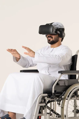 إيماءات الاندماج والتفاعل مع العالم الخيال، المتعة والتسلية بالمشاهدة عبر نظارة الواقع الافتراضي، بورترية لشاب عربي خليجي اماراتي من ذوى الاحتياجات الخاصة يرتدي الزي التقليدي و نظارات ثلاثية الأبعاد (الفي ار) يجلس على كرسي متحرك, التطور التقني والتكنولوجي ، خلفية بيضاء