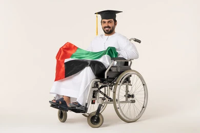 Pride in roots and national belonging, national holidays and occasions, a portrait of a young Arab Gulf Omani man with special needs wearing a dishdasha and graduation cap sitting in a wheelchair holding the Omani flag with expressions of pride, gestures of happiness and joy, white background.