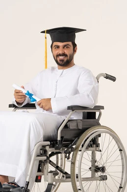 مفهوم الاجتهاد والتفوق، الشعور بالفرح والفخر والثقة بالنفس, الاحتفال بإنهاء الدراسة الجامعية، بورتريه لطالب عربي اماراتي خليجي من ذوي الاحتياجات الخاصة يرتدي الثوب الأبيض وقبعة التخرج يجلس على كرسي متحرك يمسك بيده الشهادة , النظر الى الكاميرا بإيماءات الرضا والسرور, أهمية الدراسة الجامعية والفرح بتحقيق النجاح