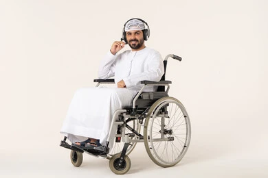 الاندماج و التفاعل مع الانغام الموسيقية، مواهب غنائية فنية، بورتريه لرجل عربي خليجي اماراتي من ذوي الاحتياجات الخاصة يرتدي الزي الاماراتي يجلس على كرسي متحرك يستمع الى الموسيقى من خلال سماعه الرأس ، النظر الى الكاميرا بايماءات السعاده و السرور ، الانصات والإستماع للأغاني بإستخدام الهيدفون، خلفية بيضاء
