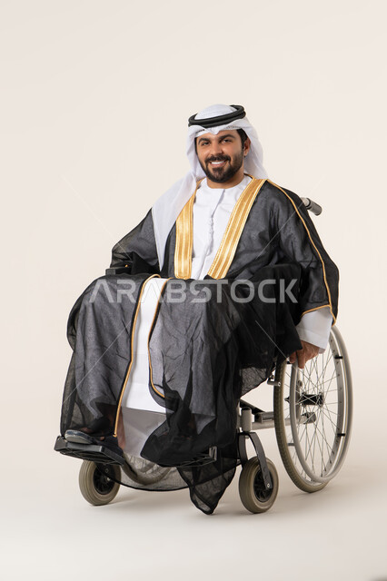 استخدام كراسي المعاقين للمساعده على الحركه والتنقل, تحسين جودة حياة ذوي الاعاقه الحركيه, بورتريه لرجل عربي خليجي الاماراتي يرتدي الزي التقليدي يجلس على كرسي متحرك ينظر الى الكاميرا بايماءات السعاده و السرور
