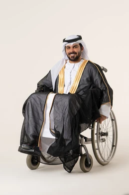استخدام كراسي المعاقين للمساعده على الحركه والتنقل, تحسين جودة حياة ذوي الاعاقه الحركيه, بورتريه لرجل عربي خليجي الاماراتي يرتدي الزي التقليدي يجلس على كرسي متحرك ينظر الى الكاميرا بايماءات السعاده و السرور