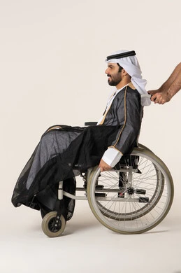 The feeling of belonging, appreciation, and respect for the disabled in Saudi Arabia, providing devices and equipment that assist with movement and mobility, caring for people of determination and securing their special needs, a side portrait of an Arab Emirati Gulf man with special needs sitting in a wheelchair, with a white background.