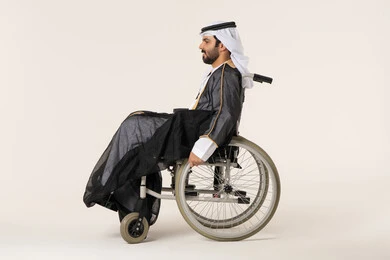 لعنايه بأصحاب الهمم وتأمين احتياجاتهم الخاصة، تأمين اجهزة ومعدات تساعد بالحركة والتنقل، بورتريه من الجانب لرجل مريض عربي اماراتي خليجي من ذوي الاحتياجات الخاصه يجلس على كرسي متحرك، شعور المعاقين بالإنتماء والتقدير والإحترام في الامارات العربية، خلفيه بيضاء