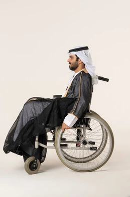 تأمين اجهزة ومعدات تساعد بالحركة والتنقل، العنايه بأصحاب الهمم وتأمين احتياجاتهم الخاصة، بورتريه من الجانب لرجل مريض عربي اماراتي خليجي من ذوي الاحتياجات الخاصه يجلس على كرسي متحرك، شعور المعاقين بالإنتماء والتقدير والإحترام في الامارات العربيه، خلفيه بيضاء