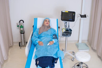 A medical follow-up session for a patient using a modern device to monitor vital signs. A veiled Emirati Gulf Arab woman lies on a hospital bed. Patients undergo regular check-ups and follow-ups.