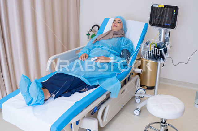 Conducting a comprehensive medical examination using an advanced electronic device that helps the medical team monitor the patient's condition during treatment. A veiled Emirati Gulf Arab woman lying in a hospital bed. Conducting examinations and periodic follow-up of patients.
