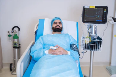 رجل يرتدي الزي الطبي موصول بجهاز لمراقبة العلامات الحيوية, مريض عربي خليجي اماراتي مستلقي على سرير في المستشفى, أجهزة ومعدات طبية في غرفة العمليات