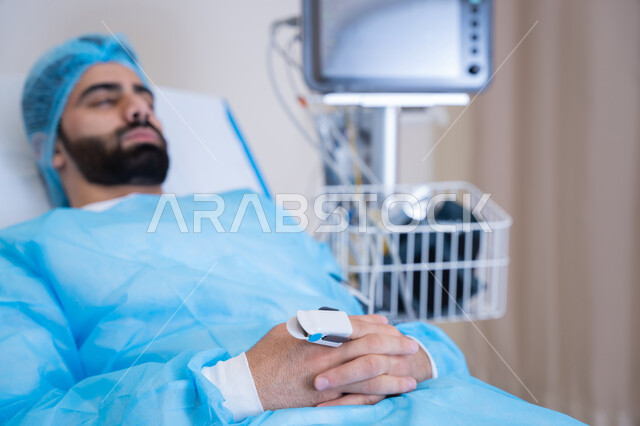 غرفة عناية يظهر فيها مريض عربي خليجي اماراتي مستلقي على السرير الطبي تحت المراقبة الطبية, عملية متابعة نبض المريض باستخدام جهاز التأكسج, الأدوات والمعدات الطبية
