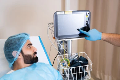 مريض عربي خليجي اماراتي مستلقي على سرير في المستشفى, مراقبة نبضات القلب, أجهزة ومعدات طبية في غرفة العمليات, طبيب يشير باصبع السبابة الي جهاز المونيتور