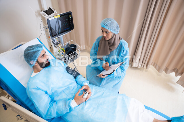 أجواء يسودها الاطمئنان والدعم النفسي قبل العلاج, طبيبة عربية خليجية اماراتية محجبة تقوم بقياس الضغط للمريض, دمج التكنولوجيا الحديثة في المجال الطبي