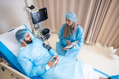 أجواء يسودها الاطمئنان والدعم النفسي قبل العلاج, طبيبة عربية خليجية اماراتية محجبة تقوم بقياس الضغط للمريض, دمج التكنولوجيا الحديثة في المجال الطبي