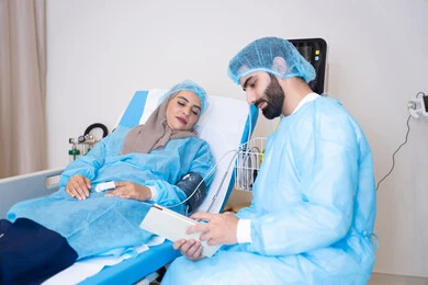 An Emirati Gulf Arab doctor and a veiled patient wearing blue surgical gowns and protective caps, measuring vital signs in the hospital, providing consultations and medical services