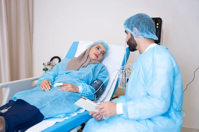 تقديم الاستشارات والخدمات العلاجية، غرفه حديثة لفحص ورعاية المرضى في المستشفى، طبيب عربي خليجي اماراتي يرتدي المريول الطبي و يقوم بقراءة نتيجة الفحوصات, مريضة محجبة مستلقية على سرير المشفى تنصت للطبيب