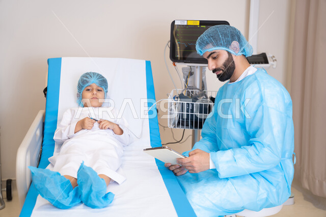 الأدوات والمعدات الطبية, دمج التكنولوجيا الحديثة في المجال الطبي، طبيب عربي خليجي اماراتي يرتدي المريول الطبي يجلس بجانب ولد مريض في المستشفى و يقوم بقياس العلامات الحيوية للمريض