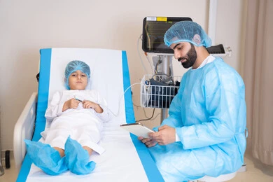 الأدوات والمعدات الطبية, دمج التكنولوجيا الحديثة في المجال الطبي، طبيب عربي خليجي اماراتي يرتدي المريول الطبي يجلس بجانب ولد مريض في المستشفى و يقوم بقياس العلامات الحيوية للمريض