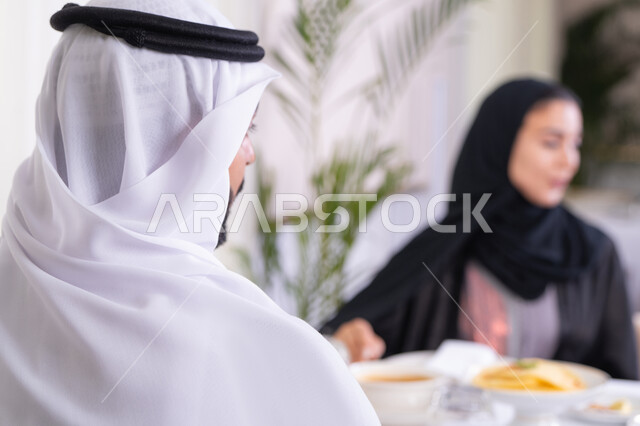 الخروج بسهرة مسائية عائلية، تقوية العلاقات الزوجية وروابط الحب والمودة، زوجان عربيان خليجيان اماراتيان يقضيان وقتهما سويا يجلسان على مائدة طعام أنيقة في مطعم راقي، يتشاركان الأحاديث والمواضيع لتقريب وجهات النظر، صورة من الخلف لرجل عربي خليجي اماراتي