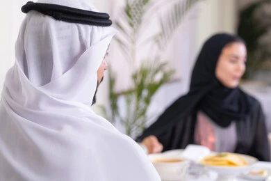 Going out for a family evening, strengthening marital relations and bonds of love and affection, an Arab Gulf Emirati couple spending their time together sitting at an elegant dining table in a high-end restaurant, sharing conversations and topics to bring viewpoints closer, background image of an Arab Gulf Emirati man