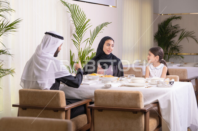 أجواء أسرية مليئة بالألفة والمحبة، التسامر والدردشة وقضاء وقت ممتع مع العائلة، عائلة عربية خليجية إماراتية يقومون بتناول الطعام، قضاء وقت عائلي ممتع في مطعم فاخر، طاولة مليئة بأطباق الأطعمة الغربية