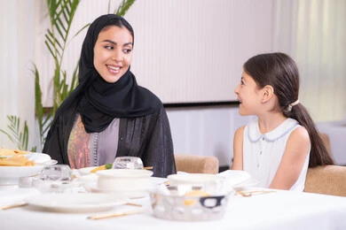 التفاهم والترابط بين الأم والطفلة، فتاه عربية خليجية اماراتية ترتدي الزي الكاجوال رفقة والدتها يقومون بتناول الطعام في مطعم راقي، تقديم الرعاية والحب للأبناء، امرأة عربية خليجية سعودية محجبة ترتدي العباءة السوداء
