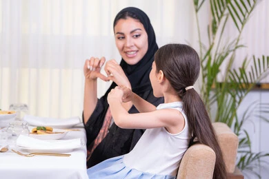 التعبير عن المشاعر لتقوية الثقة بين الأبناء والآباء، التفاهم والترابط بين الأم والطفلة، فتاه عربية خليجية اماراتية ترتدي الزي الكاجوال رفقة والدتها في مطعم فاخر، تقديم الرعاية والحب، امرأة عربية خليجية سعودية محجبة ترتدي عباءة سوداء