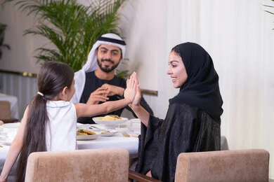 Strengthening maternal and family bonds, an Emirati Gulf Arab family eating in a fine dining restaurant, a table full of western food dishes, a slap signifying consensus and encouragement, a family atmosphere full of intimacy and love, enjoying the weekend