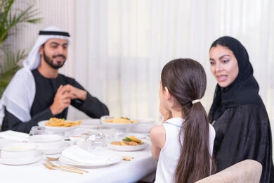 أوقات عائلية ممتعة في مطعم راقي، عائلة عربية خليجية إماراتية يقومون بمشاركة الأحاديث والمواقف الشخصية بإيماءات الاستغراب والدهشة، الاهتمام والاستماع  لمشاكل الأطفال، طاولة مليئة بأطباق الأطعمة الغربية، أجواء أسرية مليئة بالألفة، الاستمتاع في عطلة نهاية الأسبوع