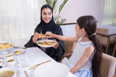 Understanding and bonding between mother and child, an Emirati Gulf Arab girl and her mother eating in a fancy restaurant, providing care and love to the children, a veiled Saudi Gulf Arab woman wearing a black abaya pouring food for her daughter Understanding and bonding between mother and child, an Emirati Gulf Arab girl and her mother eating in a fancy restaurant, providing care and love to the children, a veiled Saudi Gulf Arab woman wearing a black abaya pouring food for her daughter