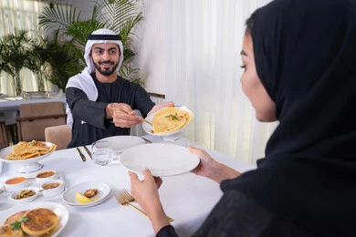 Sharing food at lunchtime, relaxing and unwinding with a family gathering, strengthening marital relations and bonds of love and affection, an Arab Gulf Emirati couple spending their time together sitting at an elegant dining table in a high-end restaurant, sharing conversations and topics to bring viewpoints closer together