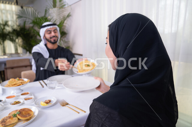 تجديد العلاقة الزوجية وتعزيز روابط الحب والمودة، مشاركة الطعام في وقت الغداء، الاستجمام والترويح عن النفس باجتماع عائلي، زوجان عربيان خليجيان اماراتيان يقضيان وقتهما سويا يجلسان على مائدة طعام أنيقة في مطعم راقي، يتشاركان الأحاديث والمواضيع لتقريب وجهات النظر