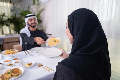تجديد العلاقة الزوجية وتعزيز روابط الحب والمودة، مشاركة الطعام في وقت الغداء، الاستجمام والترويح عن النفس باجتماع عائلي، زوجان عربيان خليجيان اماراتيان يقضيان وقتهما سويا يجلسان على مائدة طعام أنيقة في مطعم راقي، يتشاركان الأحاديث والمواضيع لتقريب وجهات النظر