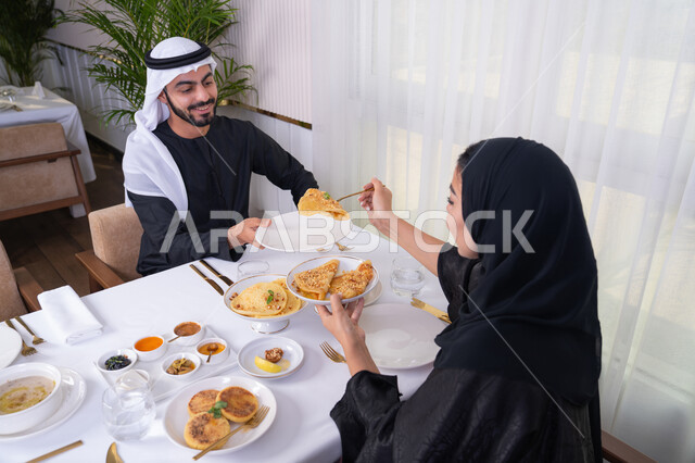 مائدة مليئة باطباق متنوعه ومختلفه من المأكولات الشهية، الألفة والمودة بين الزوجين، قضاء وقت ممتع خارج المنزل في عطلة نهاية الاسبوع, زوجان عربيان اماراتيان يقومان بتناول الطعام في المطعم, مفهوم الاسره السعيده