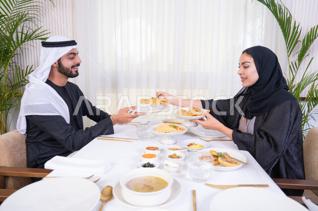 الألفة والمودة بين الزوجين، قضاء وقت ممتعه خارج المنزل في عطلة نهاية الاسبوع, زوجان عربيان اماراتيان يقوم بتناول الطعام في المطعم, مفهوم الاسره السعيده, طاولة مليئة باطباق متنوعه ومختلفه من المأكولات الشهية