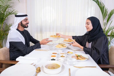 الألفة والمودة بين الزوجين، قضاء وقت ممتعه خارج المنزل في عطلة نهاية الاسبوع, زوجان عربيان اماراتيان يقوم بتناول الطعام في المطعم, مفهوم الاسره السعيده, طاولة مليئة باطباق متنوعه ومختلفه من المأكولات الشهية
