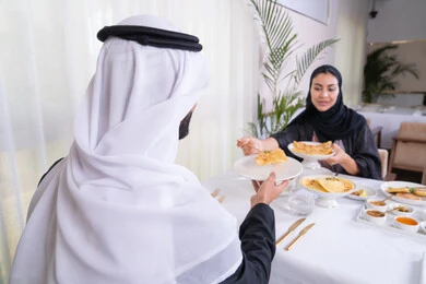 الاستمتاع في عطلة نهاية الاسبوع, مائدة مليئة باطباق متنوعه ومختلفه من المأكولات الشهية، الألفة والمودة بين الزوجين، زوجان عربيان اماراتيان يقومان بتناول الطعام في المطعم, مفهوم الاسره السعيده