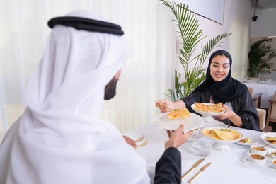 مشاركة الاطعمة بين الزوجين، مائدة مليئة باطباق متنوعه ومختلفه من المأكولات الشهية، الألفة والمودة بين الزوجين، قضاء وقت ممتع خارج المنزل في عطلة نهاية الاسبوع, زوجان عربيان اماراتيان يقومان بتناول الطعام في المطعم, مفهوم الاسره السعيده