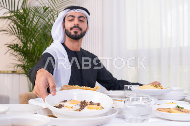 قضاء الأوقات الممتعة في الخارج, إيماءات السعادة و السرور, رجل عربي خليجي إماراتي مبتسم يرتدي الكندورة و الغترة البيضاء يجلس في إحدى المطاعم في الإمارات, أنشطة ترفيهية مسلية, الاستمتاع بالأجواء المميزة في المطعم
