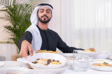 قضاء الأوقات الممتعة في الخارج, إيماءات السعادة و السرور, رجل عربي خليجي إماراتي مبتسم يرتدي الكندورة و الغترة البيضاء يجلس في إحدى المطاعم في الإمارات, أنشطة ترفيهية مسلية, الاستمتاع بالأجواء المميزة في المطعم