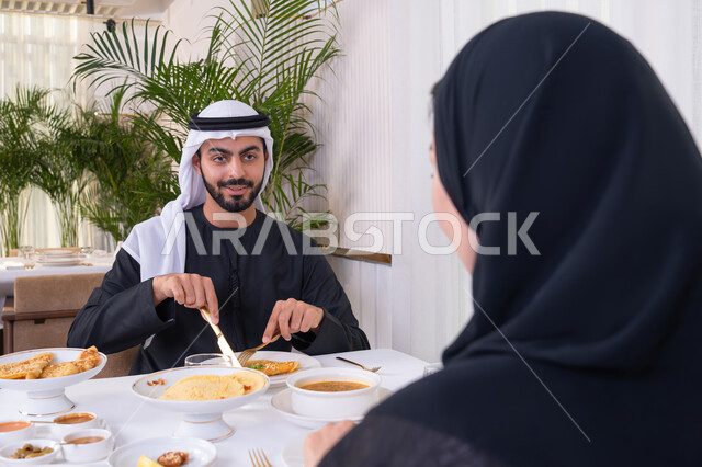 الألفة والمودة بين الزوجين، قضاء وقت ممتعه خارج المنزل في عطلة نهاية الاسبوع, زوجان عربيان اماراتيان يقوم بتناول الطعام في المطعم, مفهوم الاسره السعيده, طاولة مليئة باطباق متنوعه ومختلفه من المأكولات الشهية