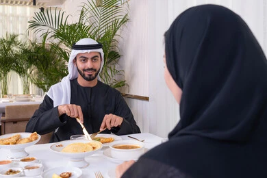 الألفة والمودة بين الزوجين، قضاء وقت ممتعه خارج المنزل في عطلة نهاية الاسبوع, زوجان عربيان اماراتيان يقوم بتناول الطعام في المطعم, مفهوم الاسره السعيده, طاولة مليئة باطباق متنوعه ومختلفه من المأكولات الشهية