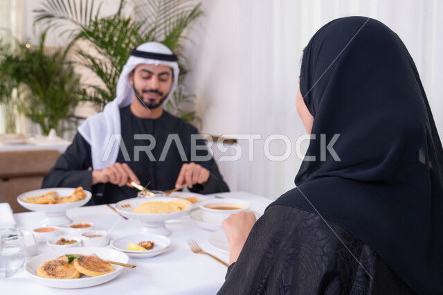 مائدة مليئة باطباق متنوعه ومختلفه من المأكولات الشهية، الألفة والمودة بين الزوجين، قضاء وقت ممتع خارج المنزل في عطلة نهاية الاسبوع, زوجان عربيان اماراتيان يقومان بتناول الطعام في المطعم, مفهوم الاسره السعيده